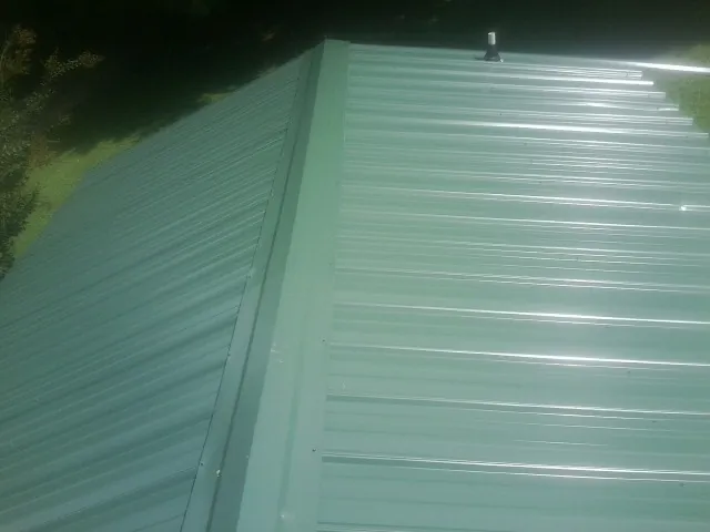 New green metal panels meeting at the ridge of a roof — Flat Roof Repair work by our crew in Ellaville