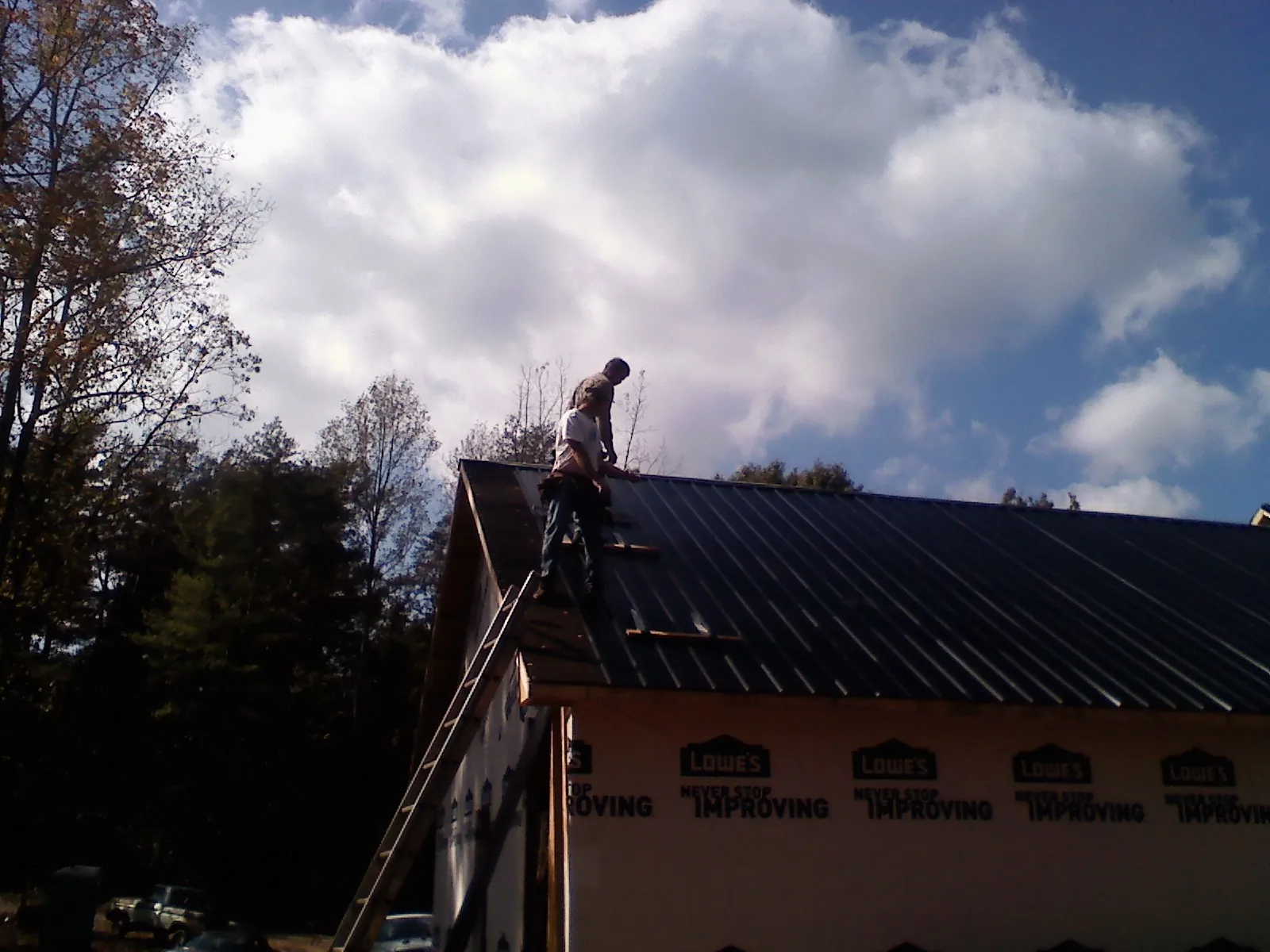Roofer fastening dark metal panels high against a cloudy sky, from a Roof Inspection job in Ellaville