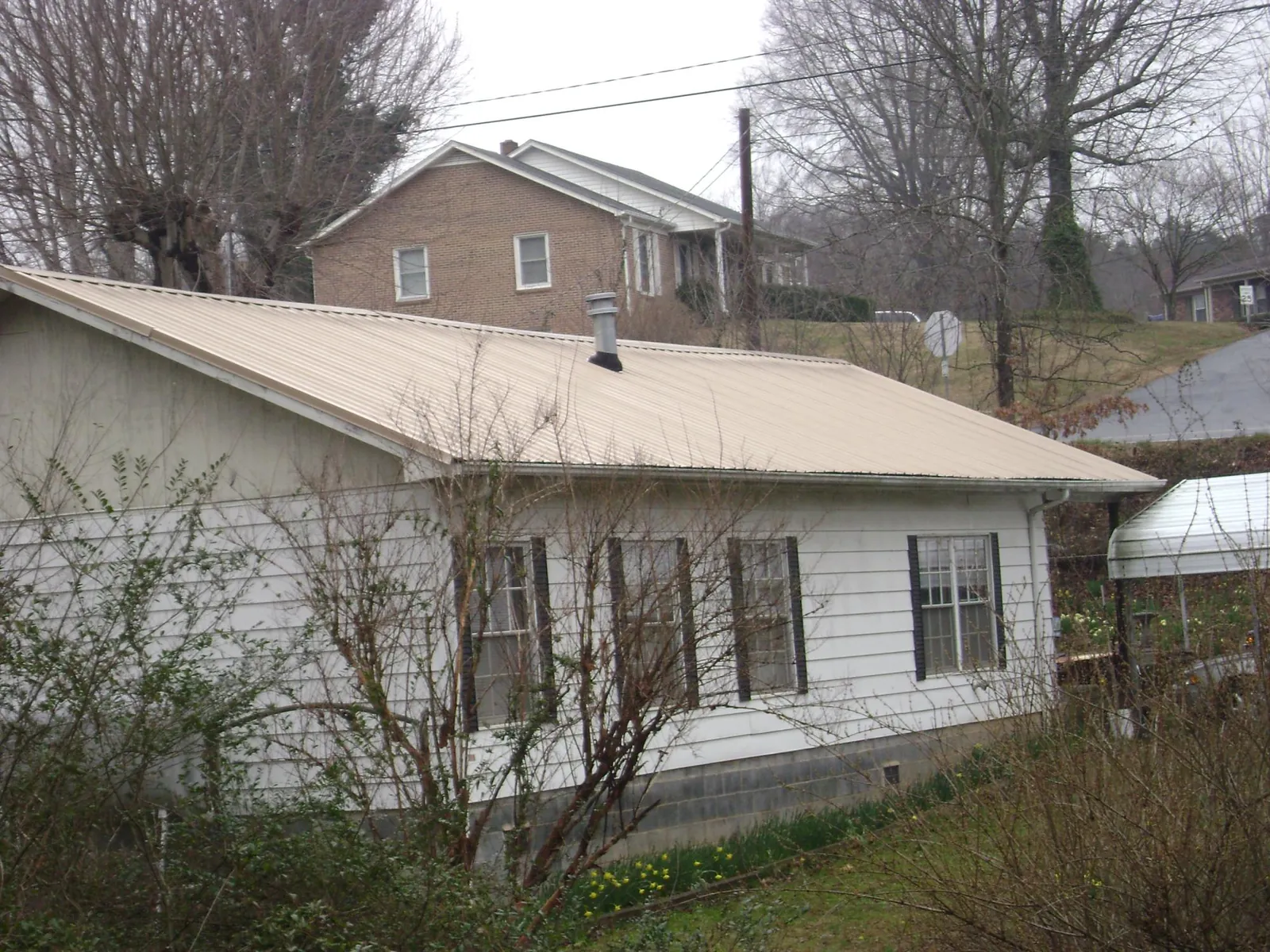 Tan metal roof on a white sided house set into a hillside — Commercial Roofing by Roofing Brothers in Ellaville