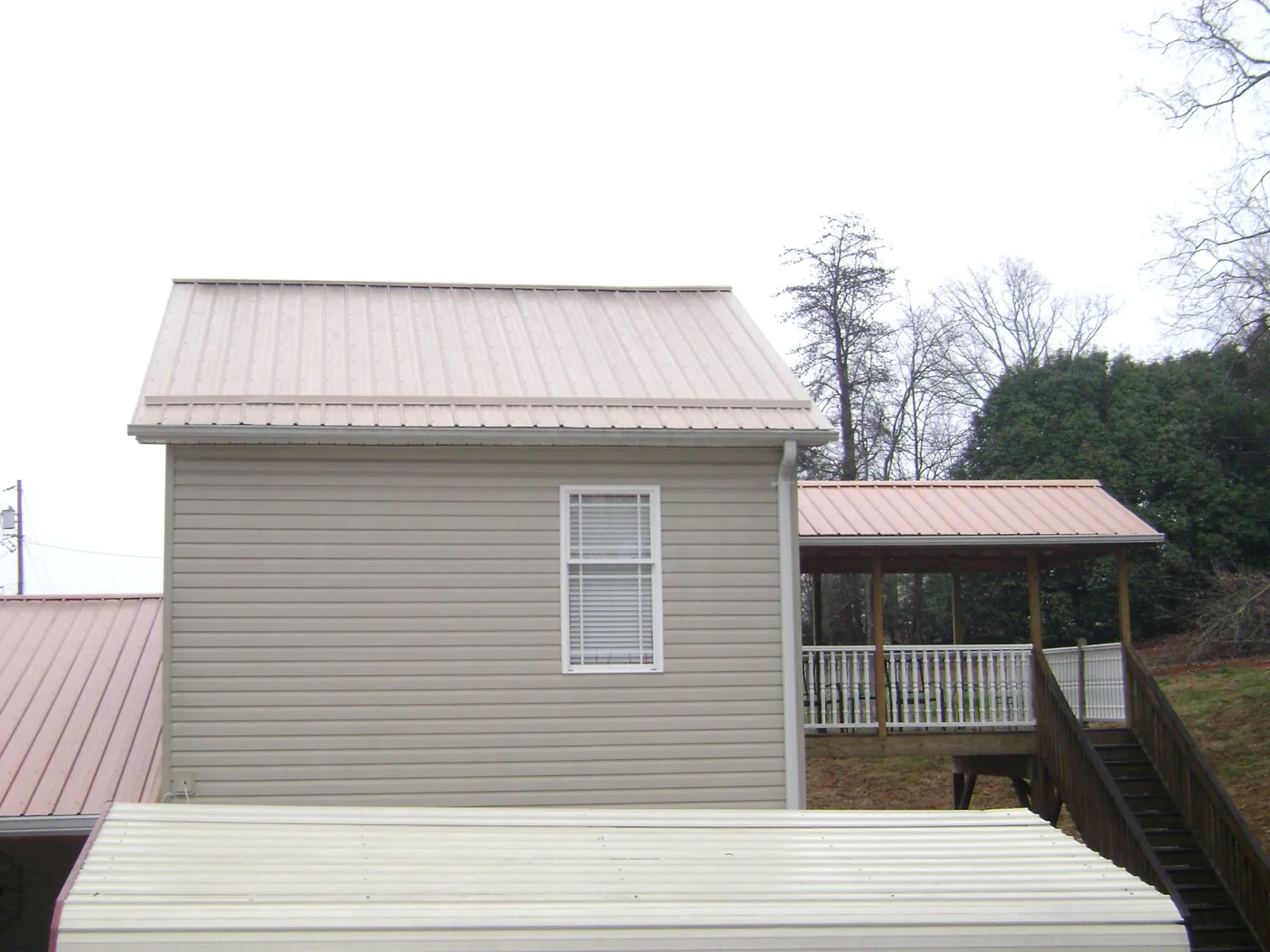 Tan metal roofs on a two story addition and attached porch, from a Roof Replacement job in Ellaville